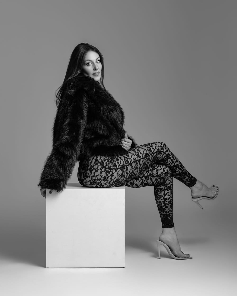 Editorial fashion pose in faux fur and lace, seated on a white plinth