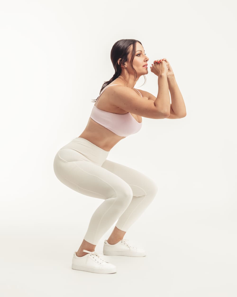 Fitness shot mid-squat in cream activewear on a white cyclorama